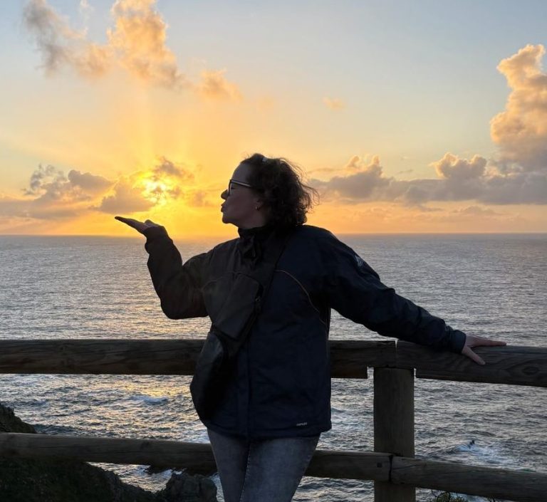 Astrid im Sonnenuntergang Fischer-Deget an Brüstungsgeländer im Abendro,t küsst die über dem Meer untergehende Sonne